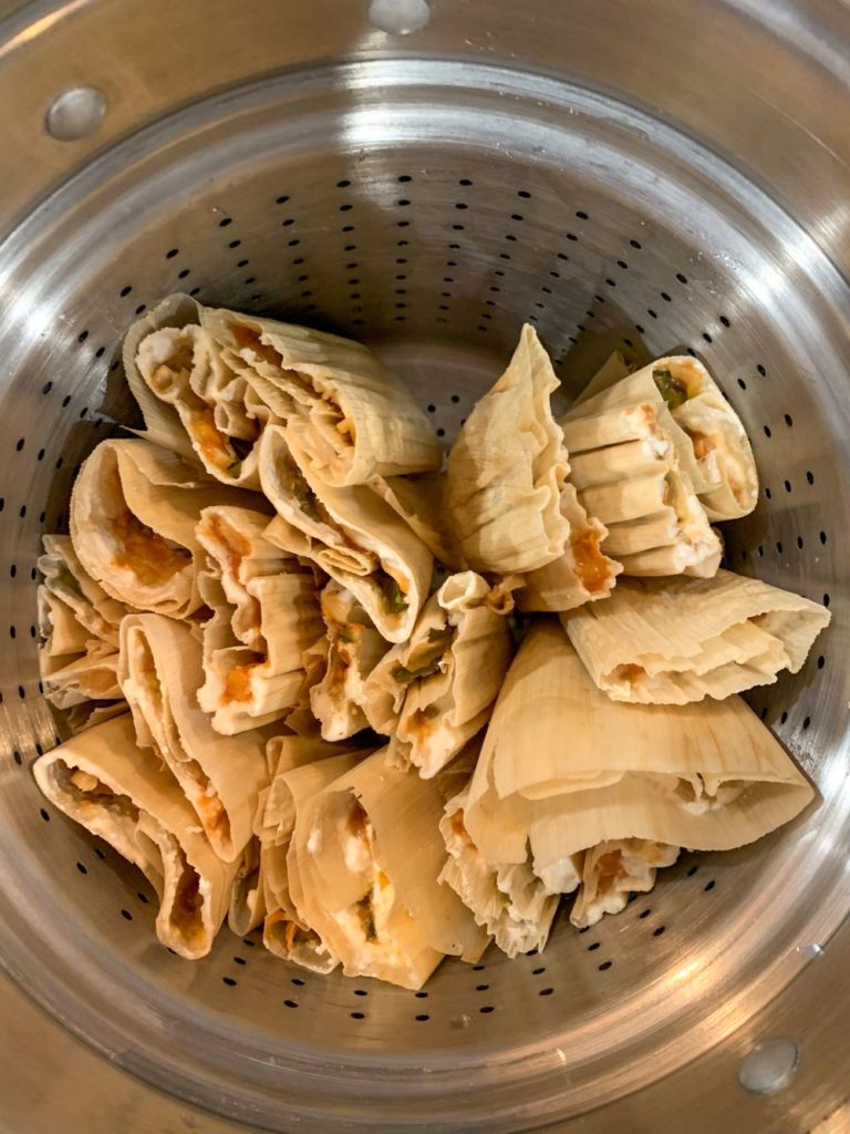 Raw tamales open end facing up in a large steamer pot